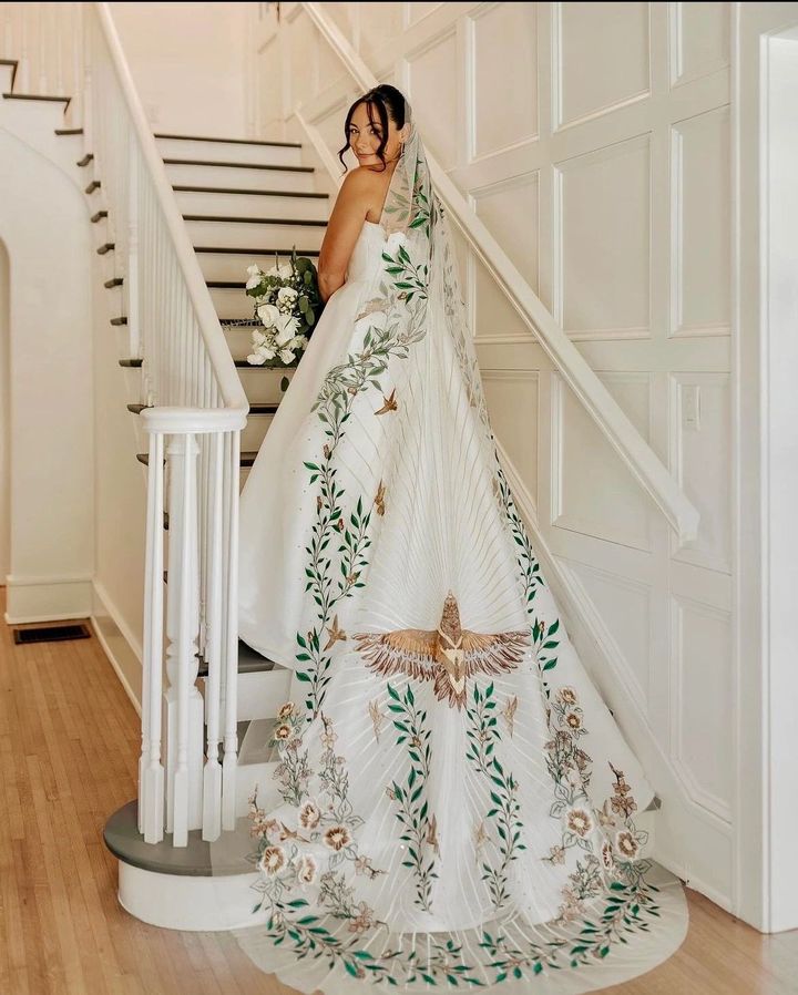 A bride on a staircase in a long white veil hand-embroidered with greenery and a bird