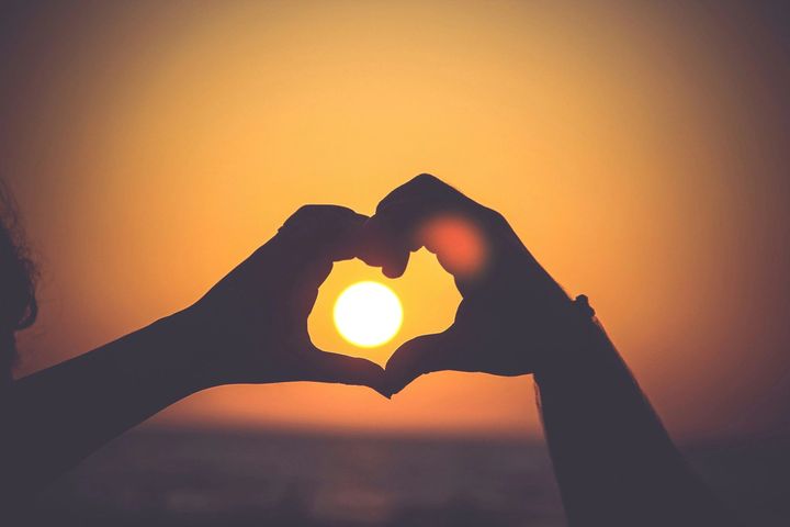 Two hands making a heart shape against an orange sunset