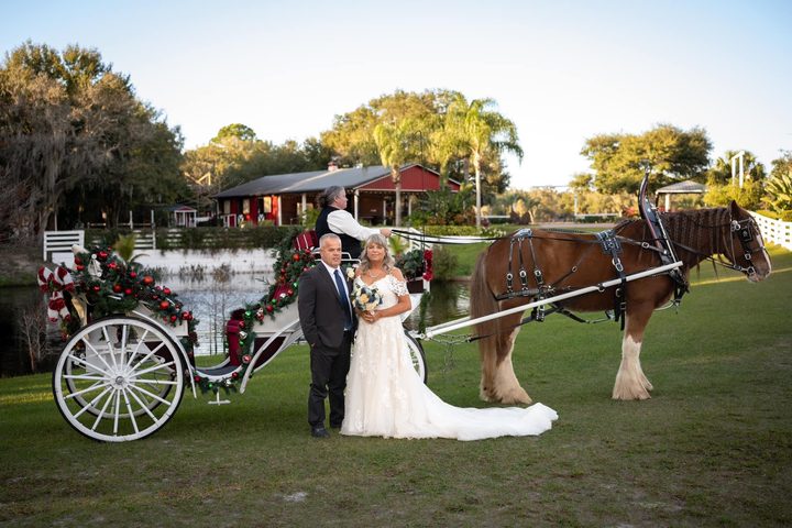A couple beside a white horse-drawn carriage on a lakeside lawn