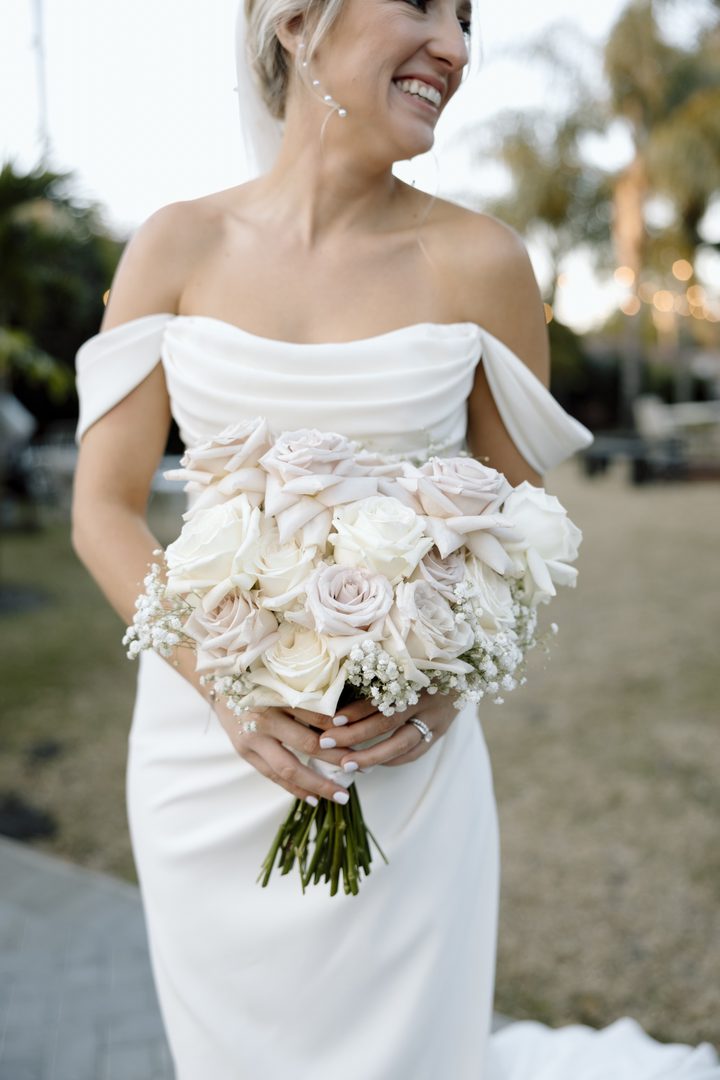 A laughing bride holding a bouquet of white and blush roses