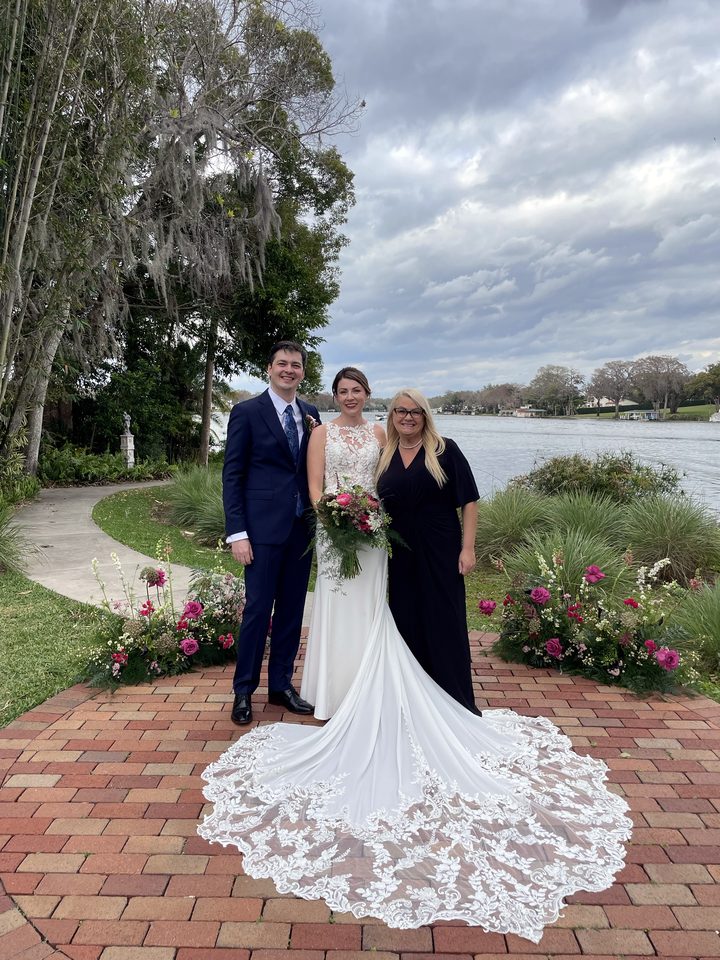 Karin with a couple on a brick terrace by a lake, the bride's lace train spread out in front