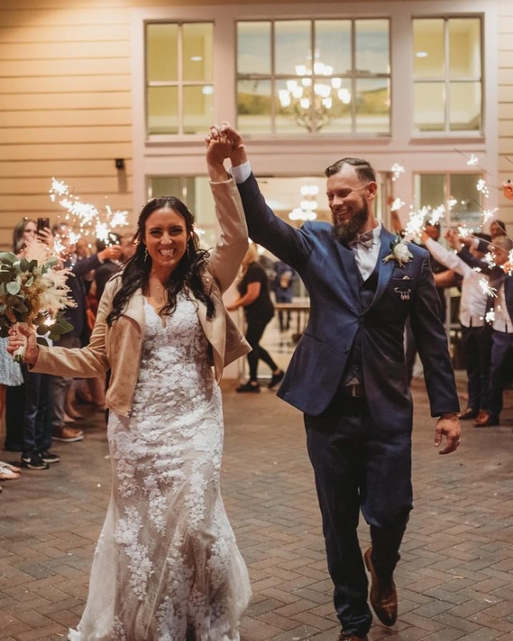 Newlyweds raise their joined hands through a sparkler send-off at night
