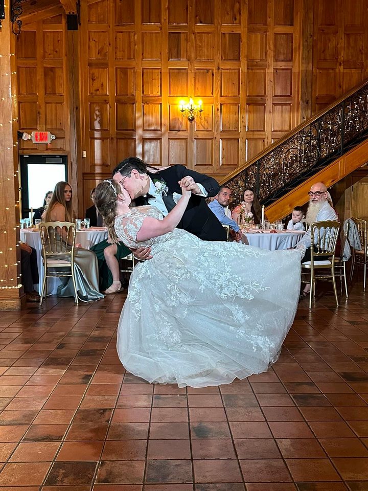 The groom dips the bride during their first dance in a wood-paneled hall