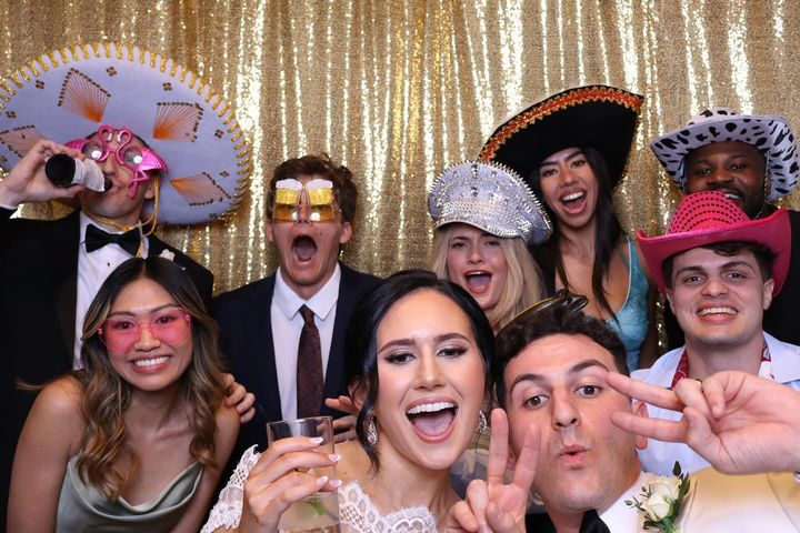 Friends pile into the photo booth in sombreros, cowboy hats and novelty glasses against a gold sequin backdrop