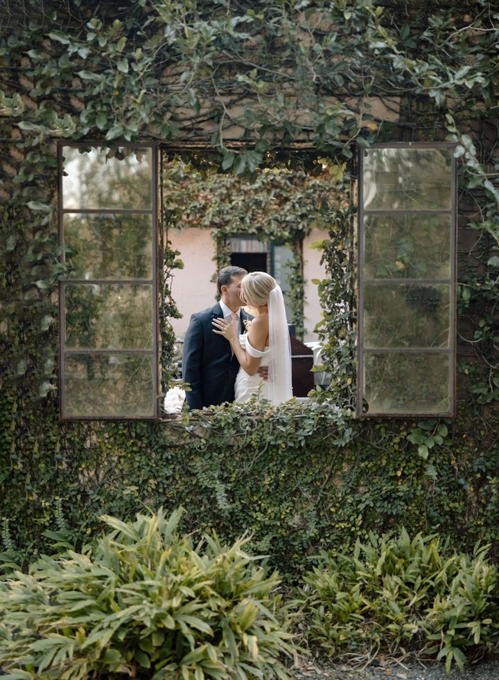 A couple kissing, seen through an open window in an ivy-covered wall