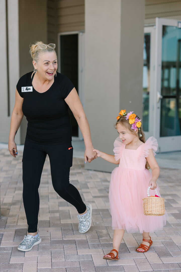 Karin, founder of Hearts & Souls, laughing as she leads a flower girl in a pink tulle dress and floral crown to the ceremony