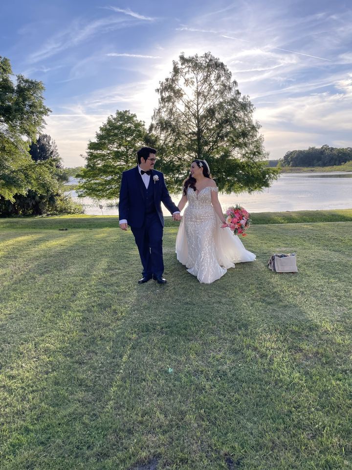 A couple walking hand in hand across a lakeside lawn at sunset