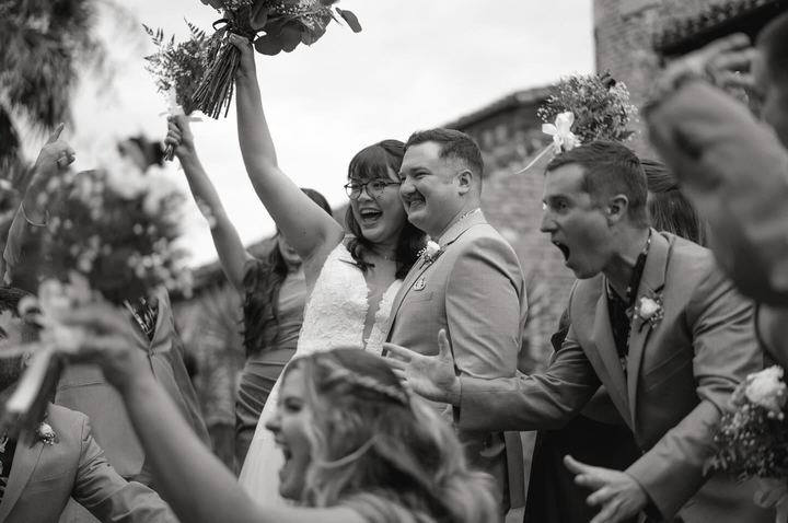 Black and white photo of the wedding party cheering around the couple