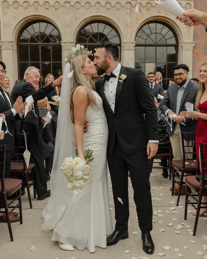 Newlyweds kiss in the aisle as guests toss white rose petals
