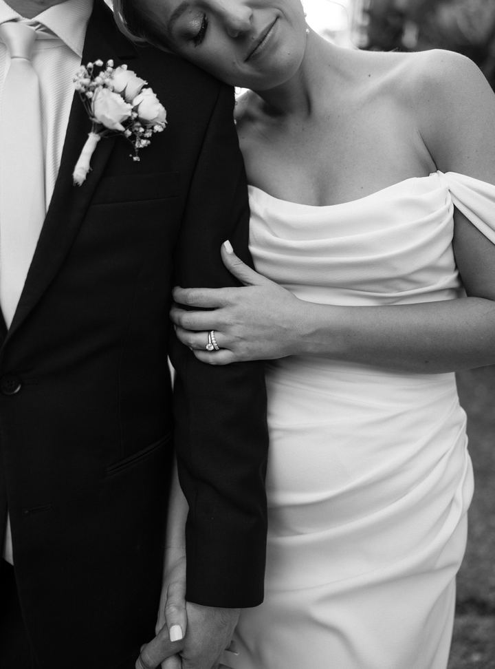 Black and white close-up of the bride resting her head on the groom's shoulder, her rings in focus