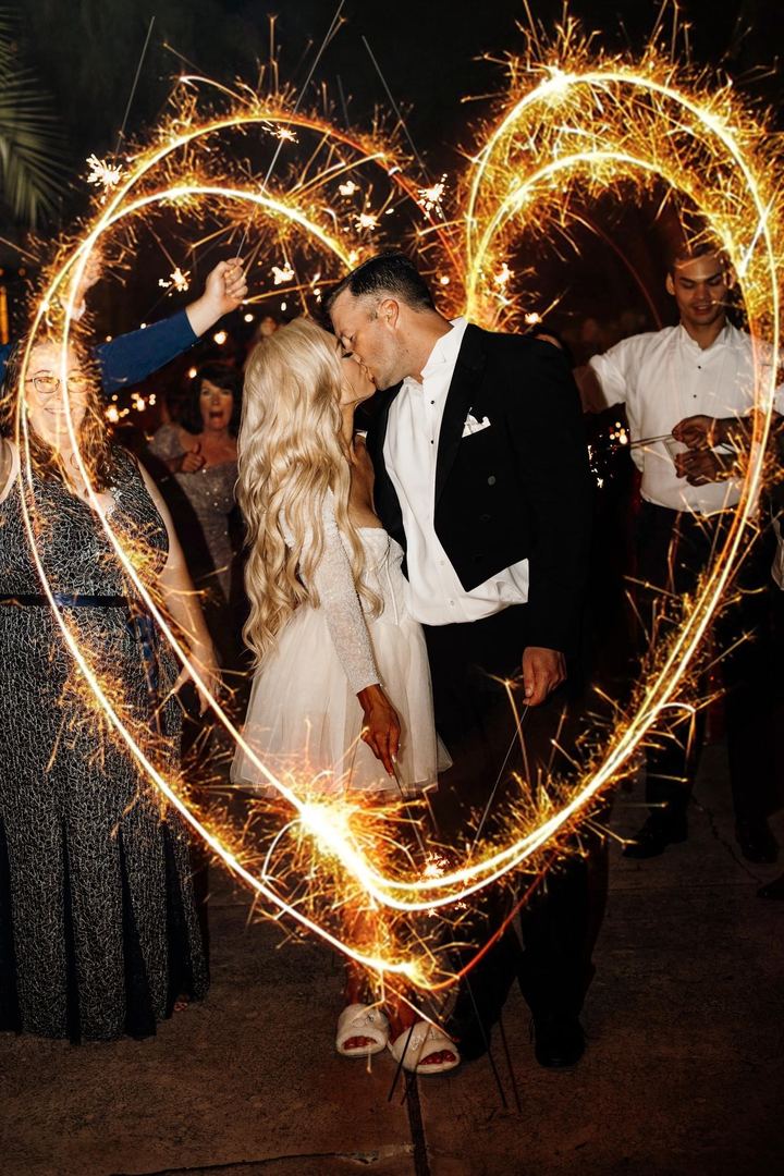 A couple kisses inside a heart traced with sparklers as guests look on