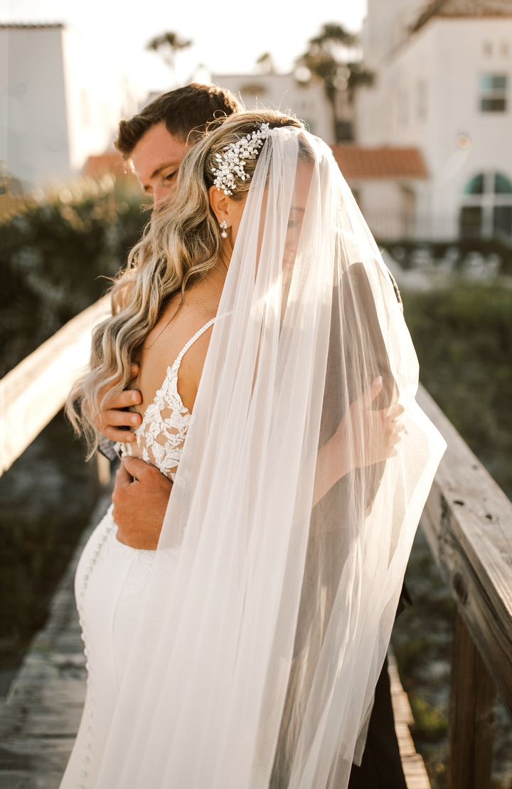 The groom embraces the bride from behind, her veil glowing in the afternoon sun