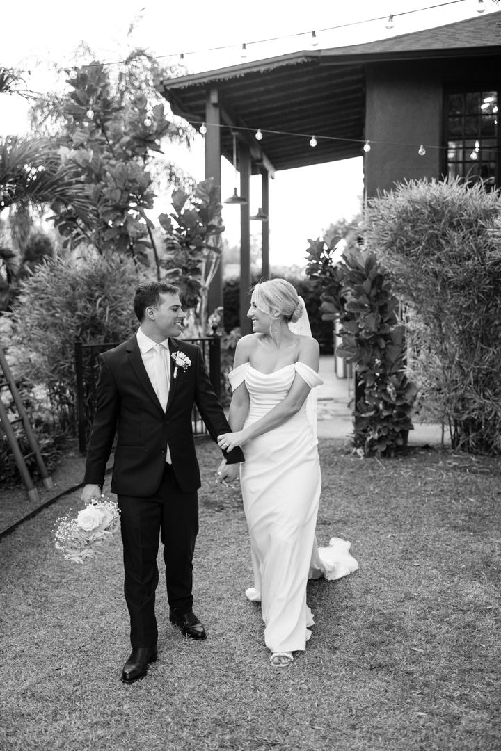 Black and white photo of a couple walking hand in hand beneath string lights